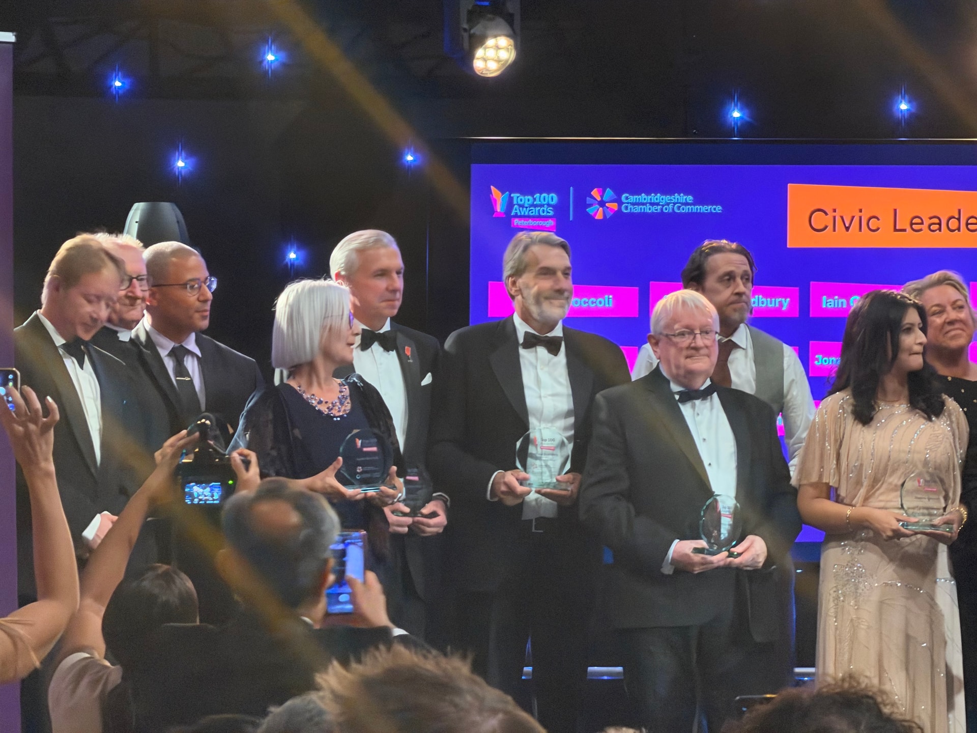 Top 100 award recipients holding glass trophies on stage